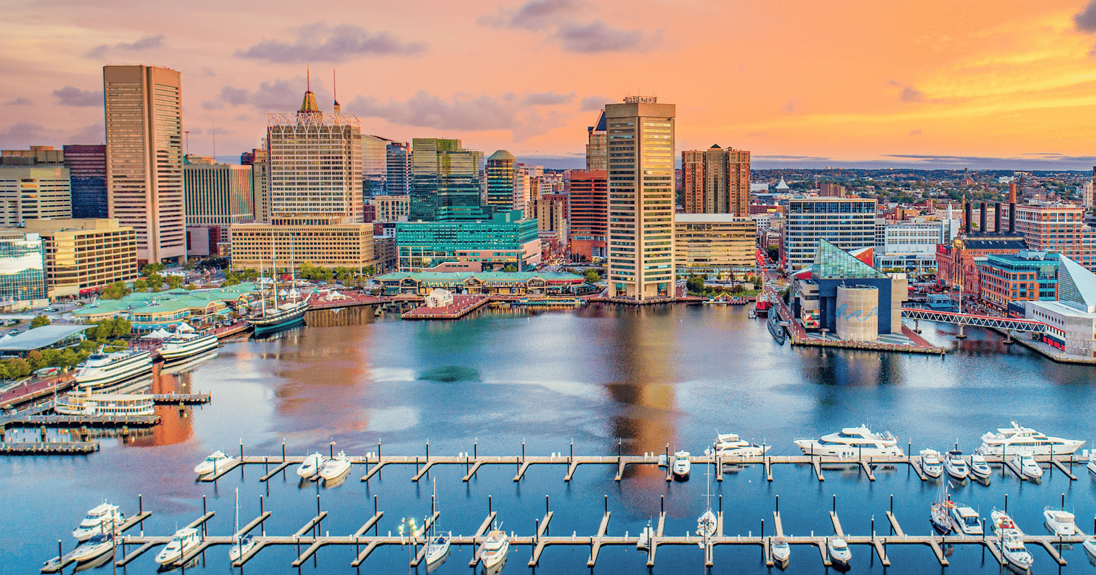 The city of baltimore at sunset with boats docked in the harbor.