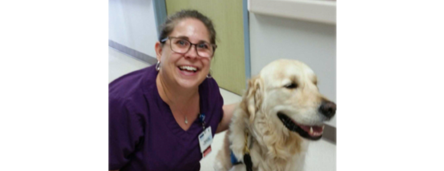Photo of nurse Rebecca smiling with golden Labrador retriever in hospital
