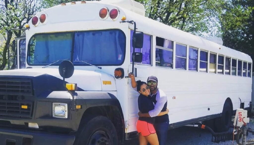 Image: Traveling Healthcare worker, Ryan King, posing wife in front of school bus turned mobile home