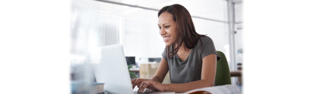 Image of woman smiling as she uses her laptop in the office