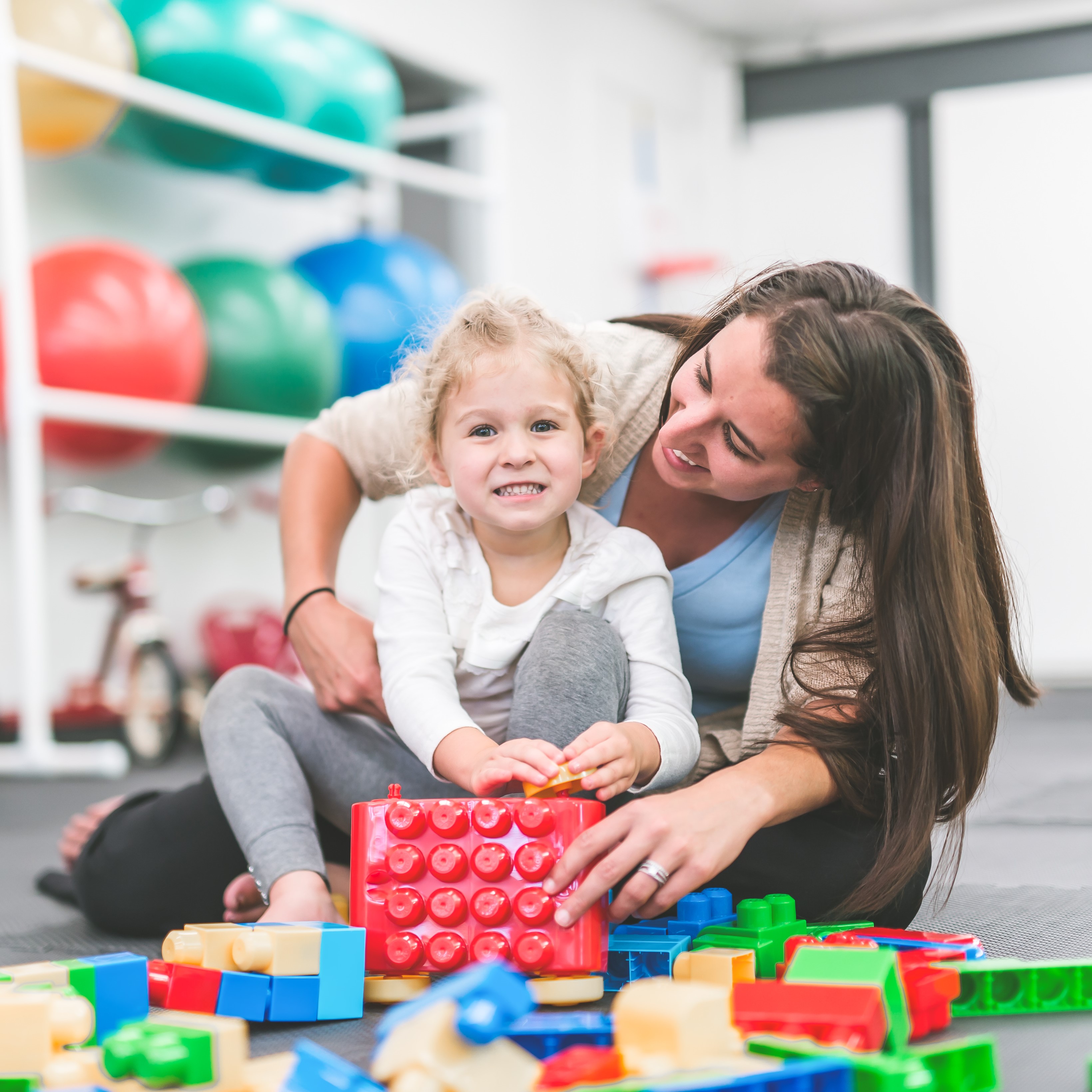 A female occupational therapist helping to rehabilitate a child patient, improving the child's motor skills by having them play with toys.
