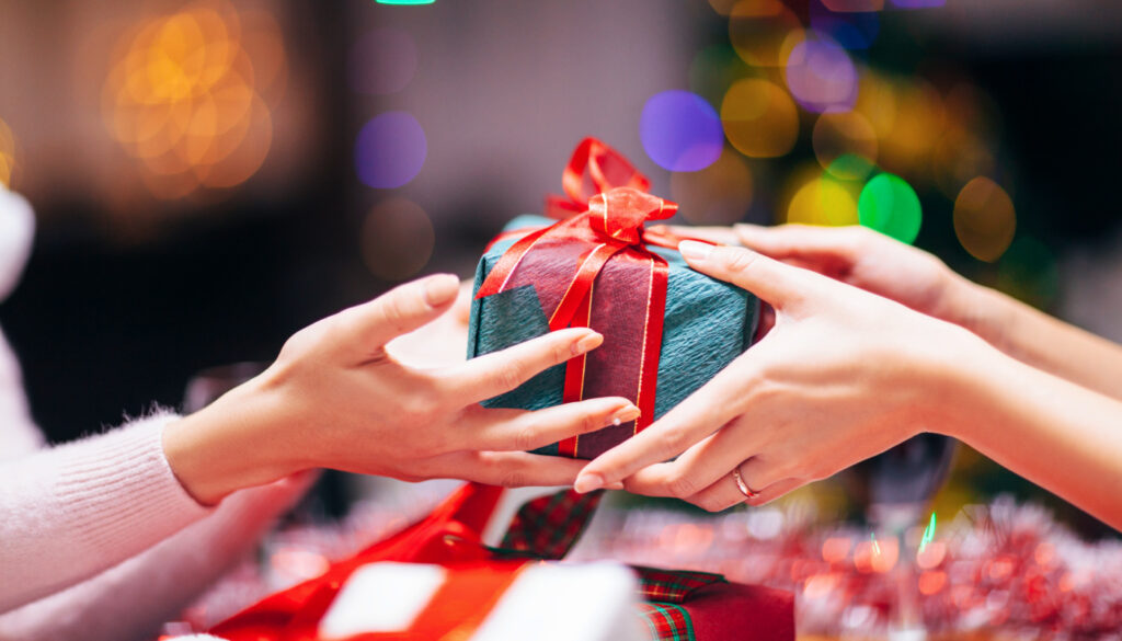 Image: Woman giving a gift to another woman for the holidays, representing holiday healthcare gift-giving.