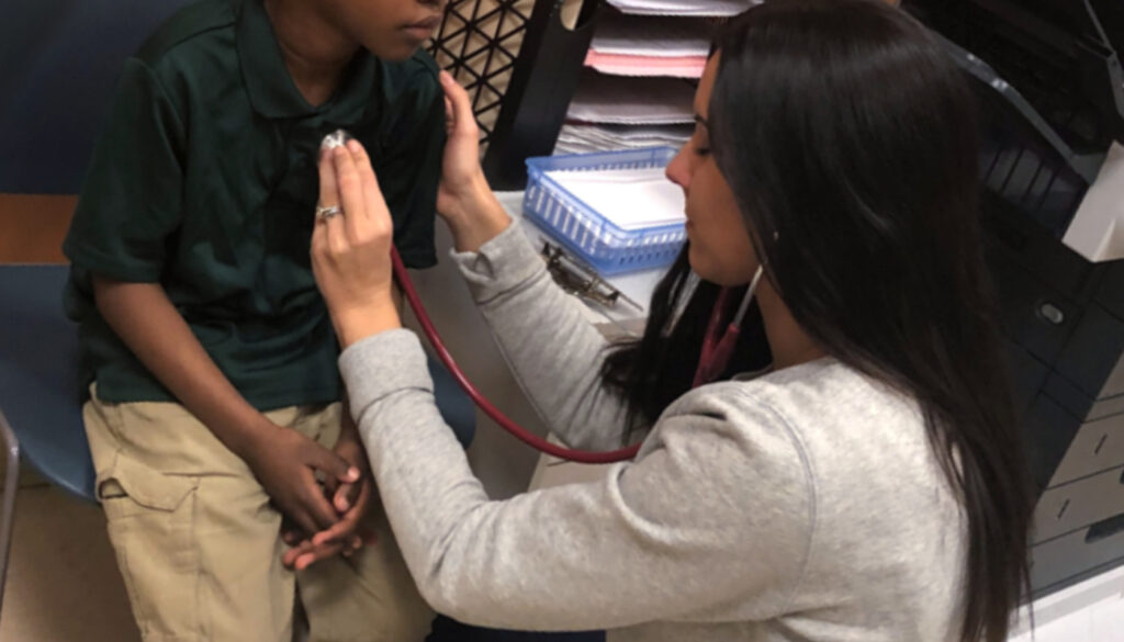 Image: Care More Spotlight showing school nurse, Brianna Perry, checking the heartbeat of a student.