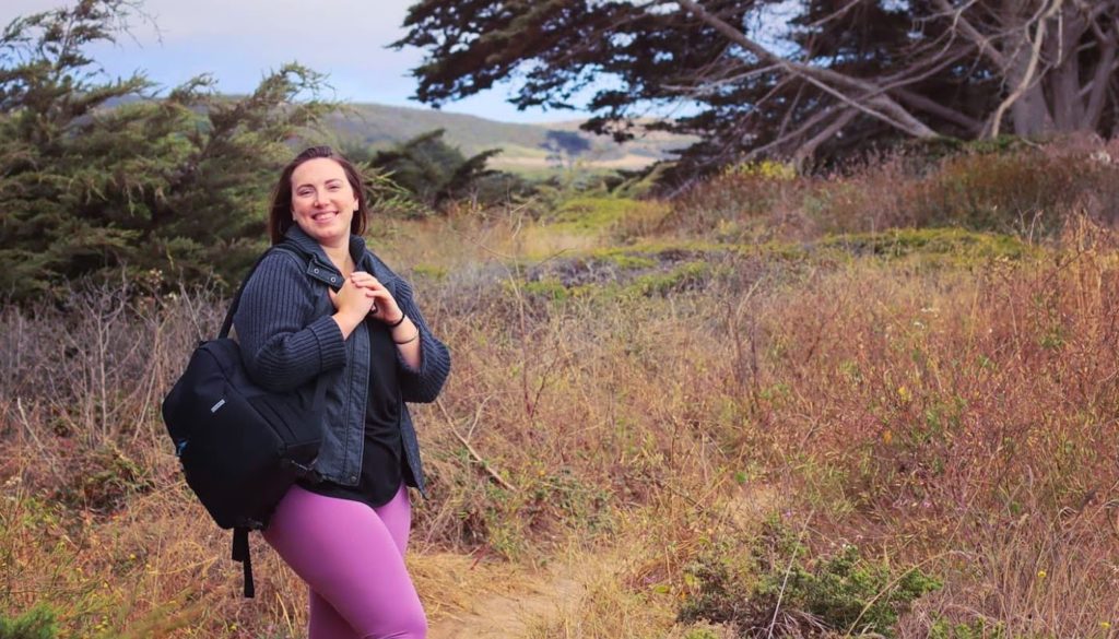 Photo of Jessie Johnson smiling for camera as she backpacks through the woods