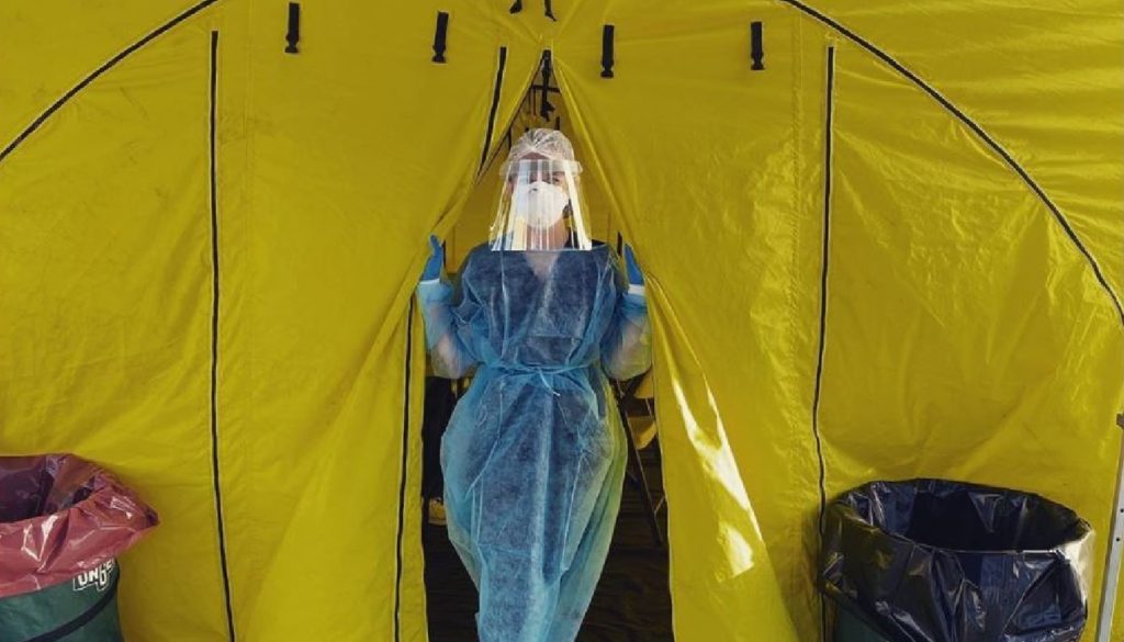 image of travel nurse Kayla posing in full ppp gear outside entrance to Covid-19 triage tent