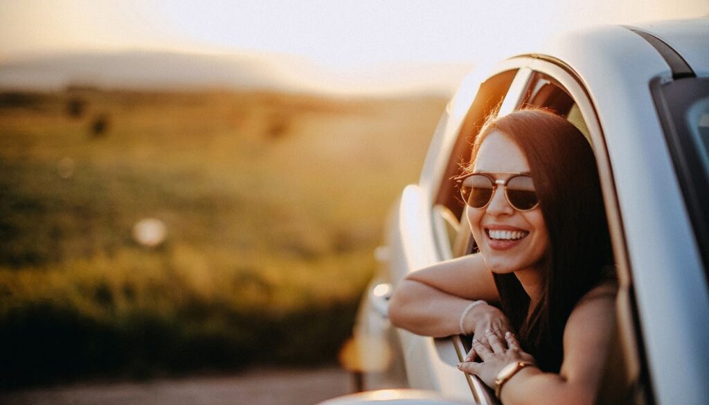 Image: Woman smiling at camera from a car ready to travel.
