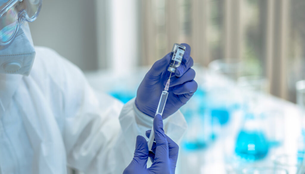 Image of healthcare lab scientist drawing a solution from a vial with syringe, depicting COVID-19 Vaccination development