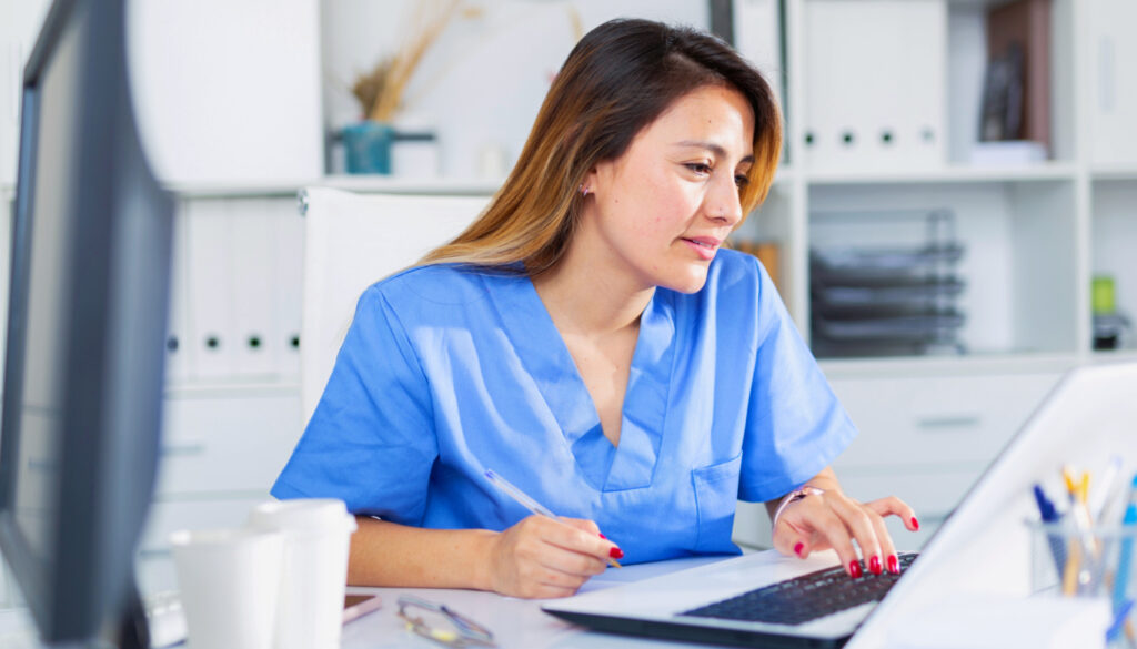 Portrait of young latina female doctor working on laptop in clinic office