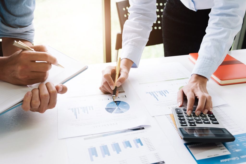 image of two pair of hands using a calculator, scanning charts and writing notes