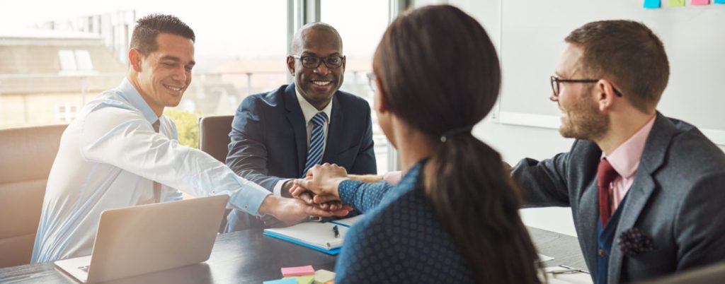 image of four executives at a table stacking their hands together while smiling