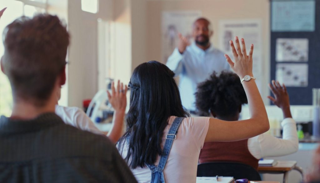 image of students in class raising their hands for the teacher