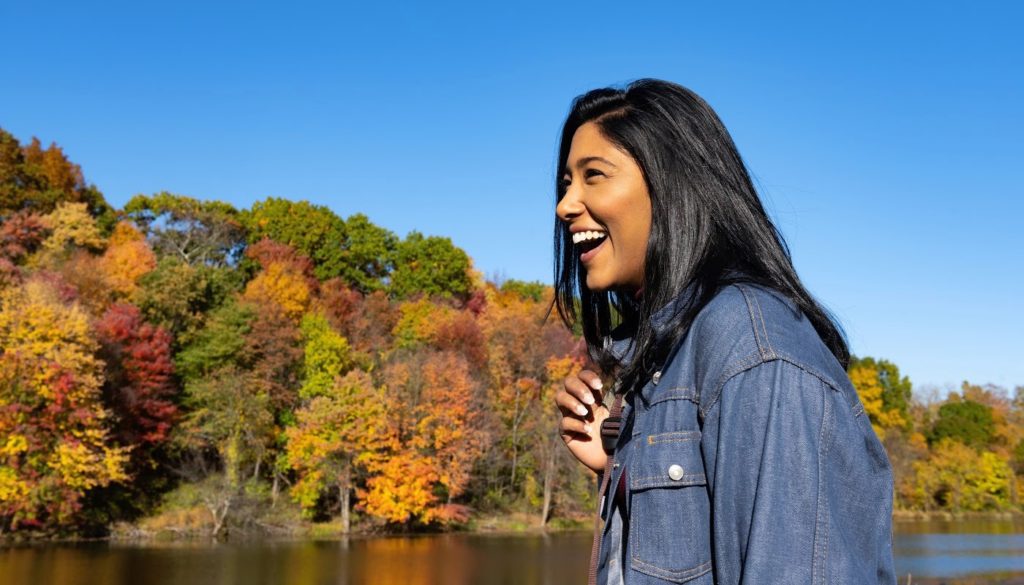 A close-up image of a woman smiling as she walks across a park in New York State as a traveling Nurse