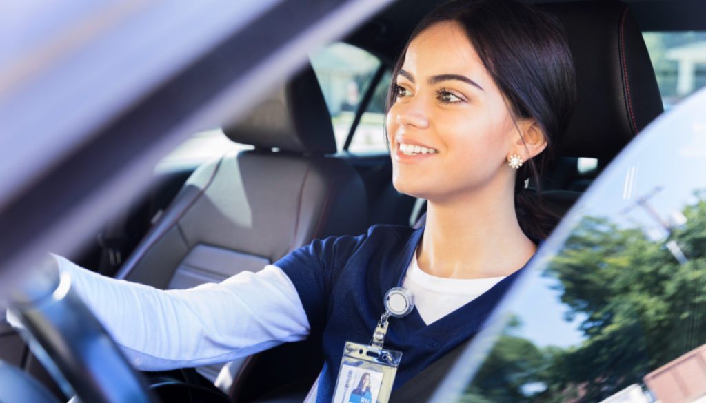 An image of a young nurse in her car smiling and ready to travel