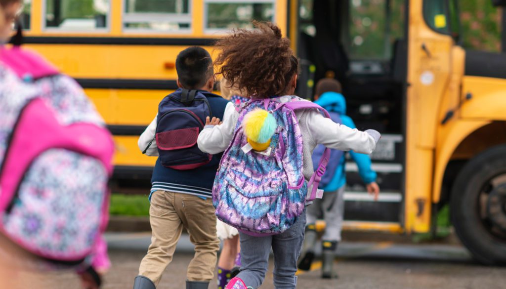 Photo of a group of young kids running into their opened schoolbus