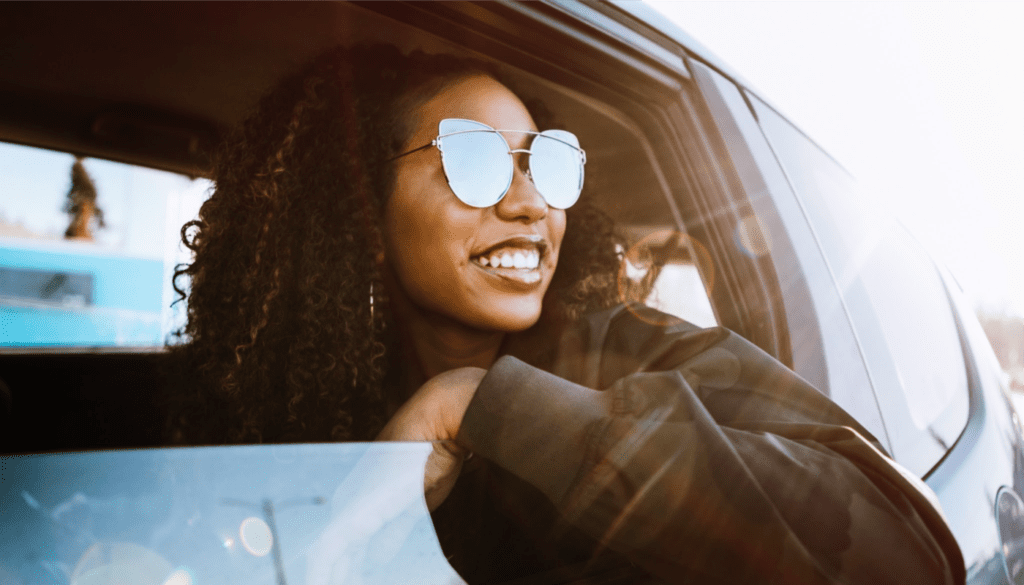 An image of a young woman in a car smiling away from the camera out her window as she travels for her healthcare job