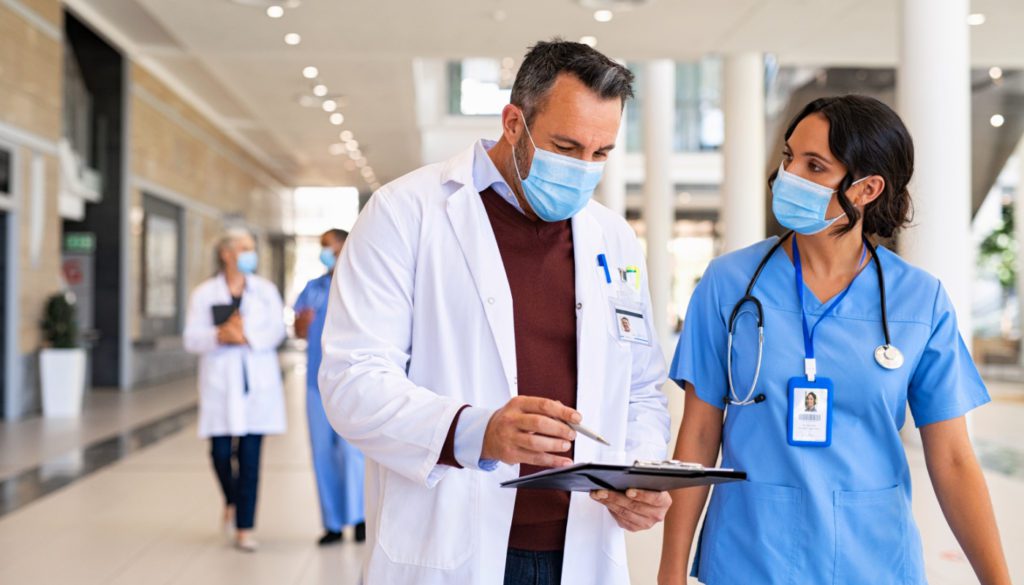 An image of a doctor and nurse discussing a medical chart while wearing masks.