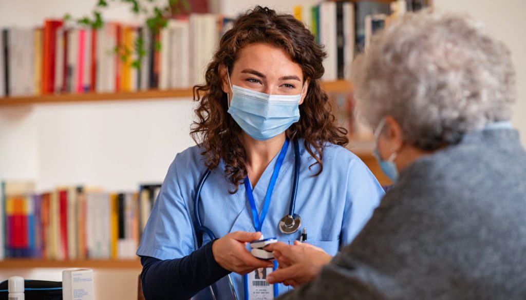 Image of a home health nurse in her scrubs and mask taking the oxygen reading of her elderly patient