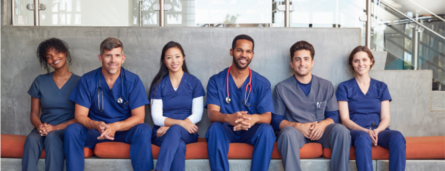 A photo of a group of young nurses sitting on a hospital bench smiling towards camera