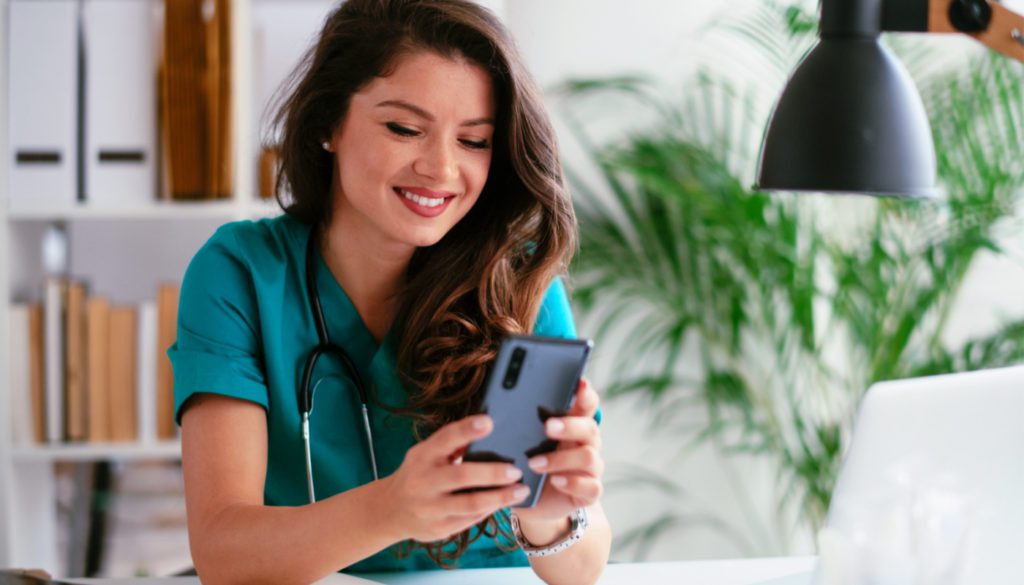 image of a nurse smiling while using her phone at a desk