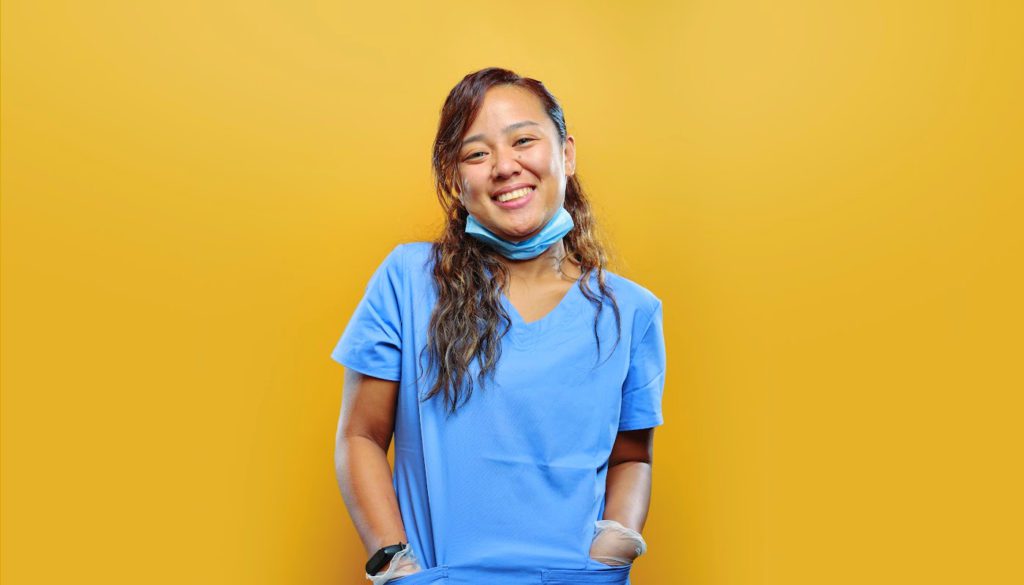 Image of a young nurse smiling while standing in front of a yellow background