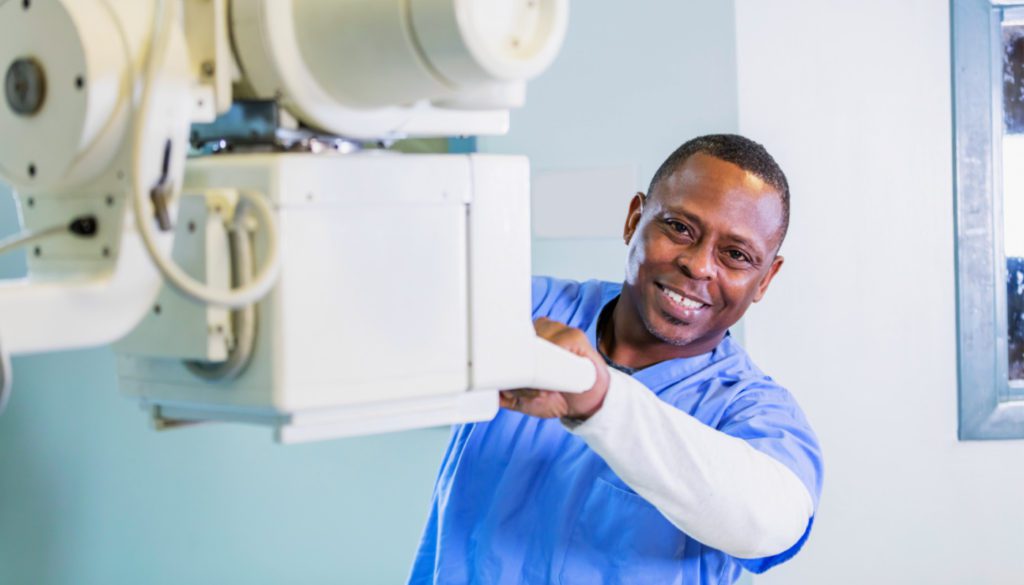 A photo of a healthcare technologist smiling while positioning a radiological machine.