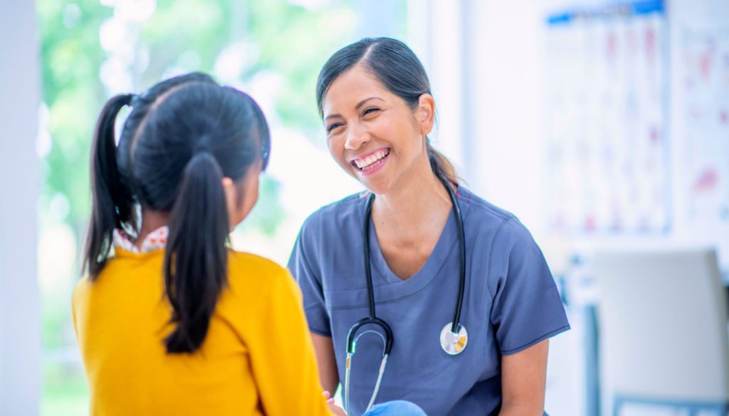 Image of a nurse smiling while she attends to a little girl at school