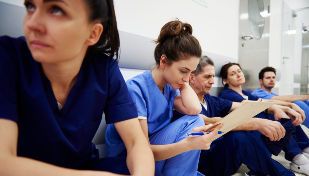 Candid image of several nurses sitting by a wall on a hospital floor visibly exhausted