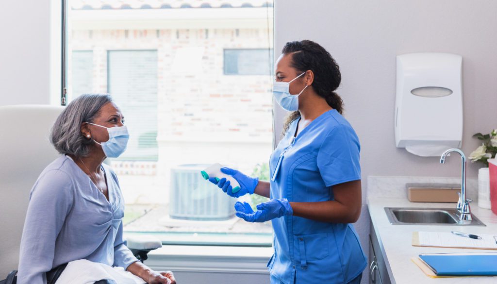 image: medical professional wearing a mask, about to take the temperature of an elderly patient in a doctor's office
