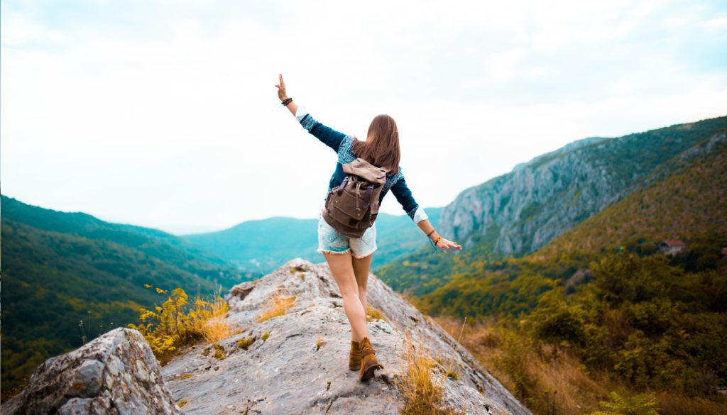 Image: hiker balancing on narrow cliff overlooking mountain range