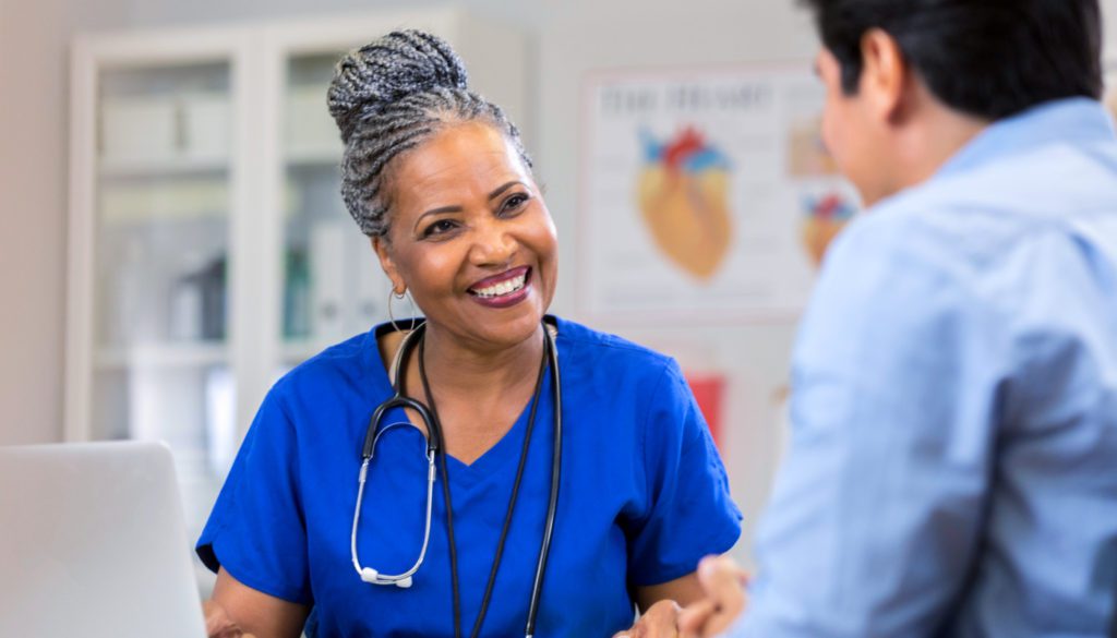 image: medical professional in her scrubs smiling as she speaks with a patient