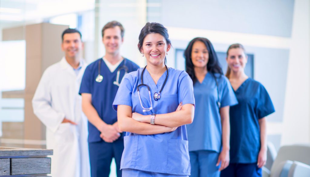 image: group of 5 medical professionals in their uniforms standing and smiling at the camera