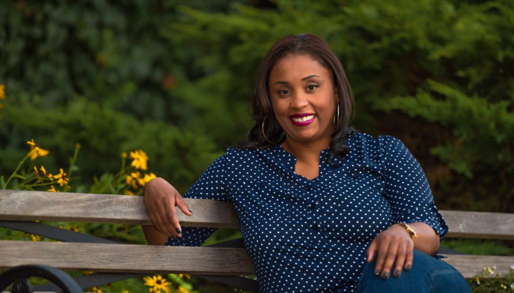 image: kelly byrd smiling as she poses on a park bench