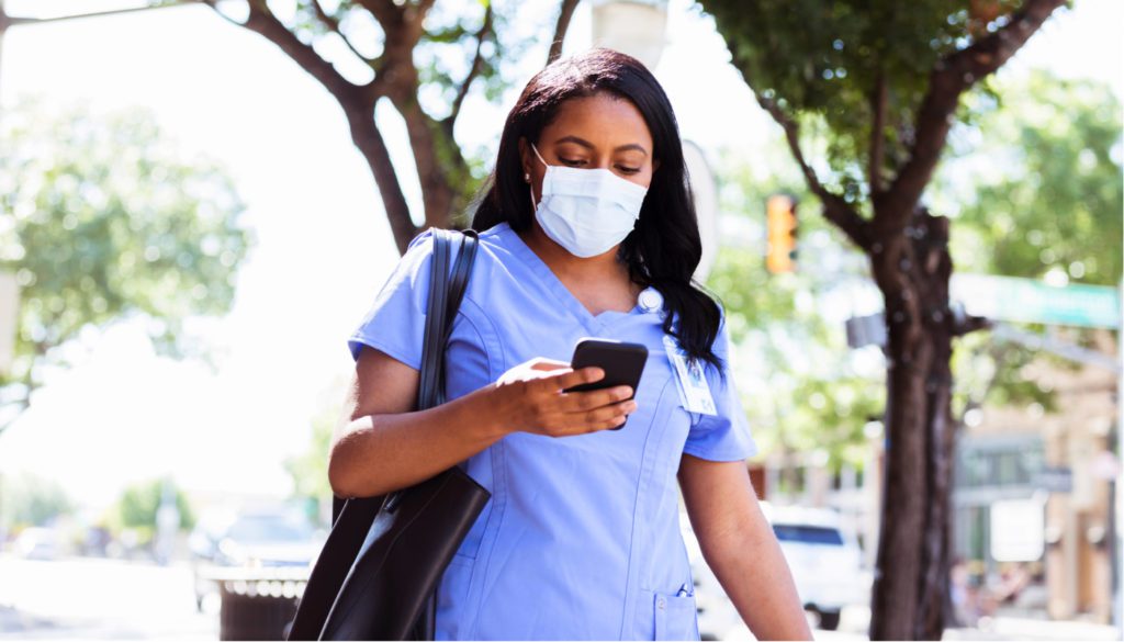 Image: nurse walking, with a face mask, looking at phone
