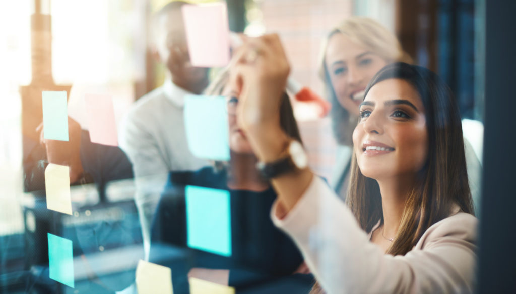 Image of woman executive presenting on a clear board to her colleagues