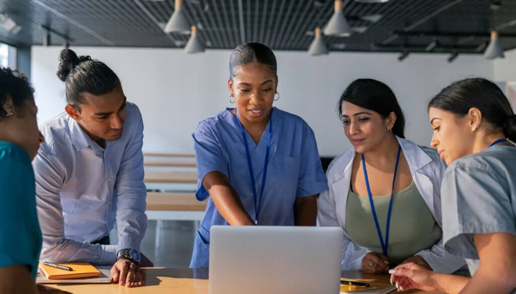 Image of a nurse showing information on a laptop to other nurses, depicting life as a nurse Manager.