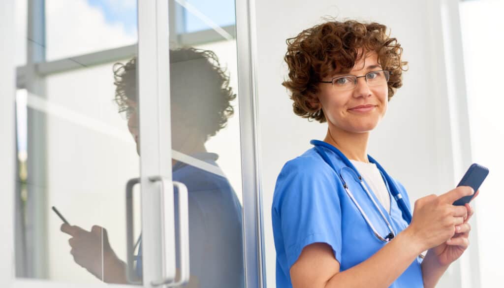 Image of a nurse smiling with phone in hand while using Supplemental Health Care's "WE Connect" Jobs app. The mobile app for nurses and healthcare professionals.