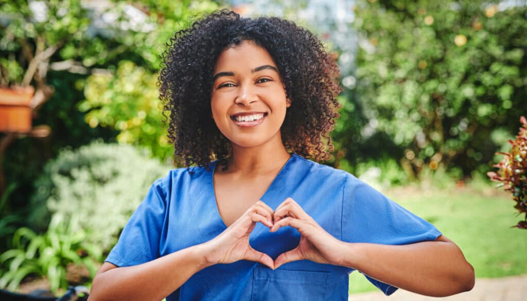 Image of woman nurse smiling towards camera making a heart gensture over her heart with her hands
