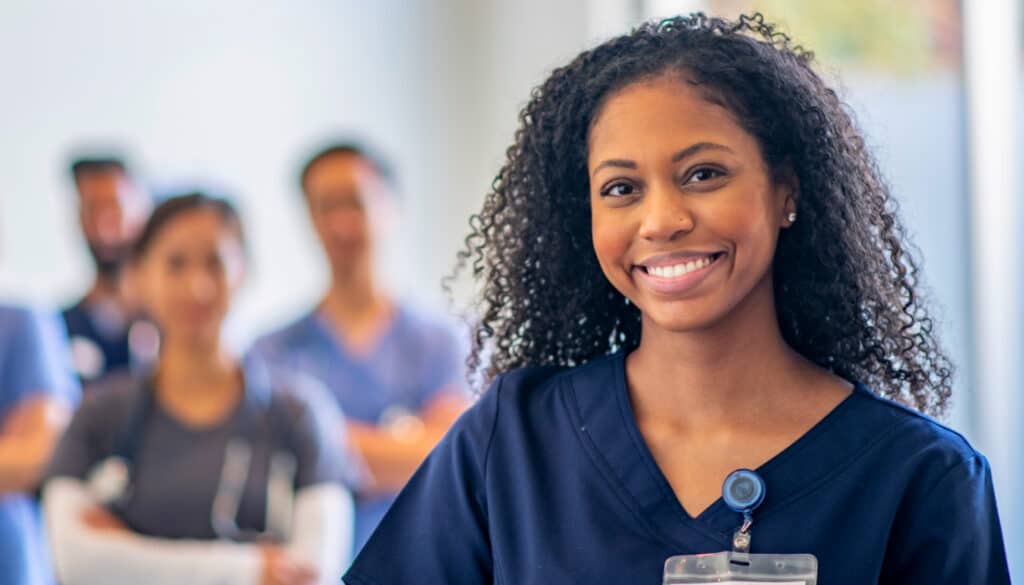 Image: Nurse smiling towards camera in the foreground, with nurses standing in the background out of focus