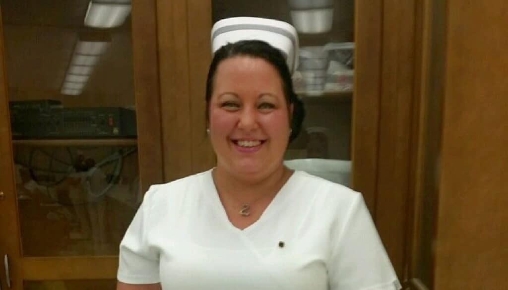 A caring nurse in a white uniform smiles in front of a cabinet, transitioning from LPN to RN.