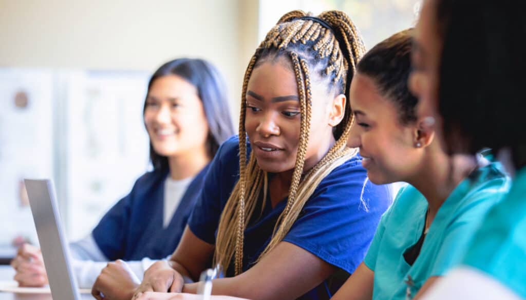 A group of CNA nurse students sitting around a table looking at a laptop.