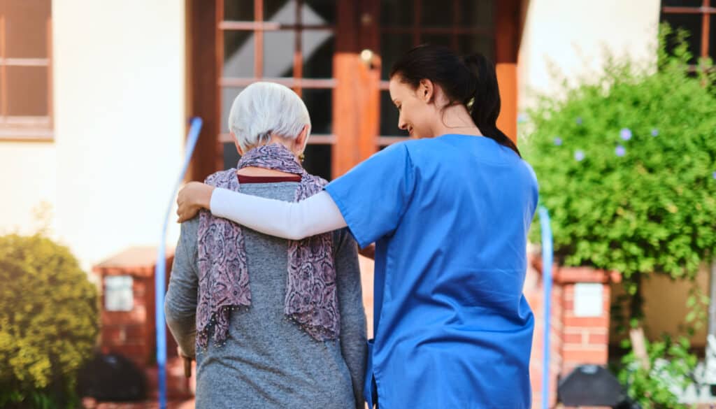 A nurse is helping an elderly woman out of the house.