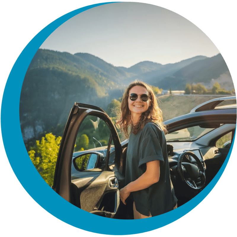 A travel nurse traveling in the mountains next to a car on a travel nursing road trip.