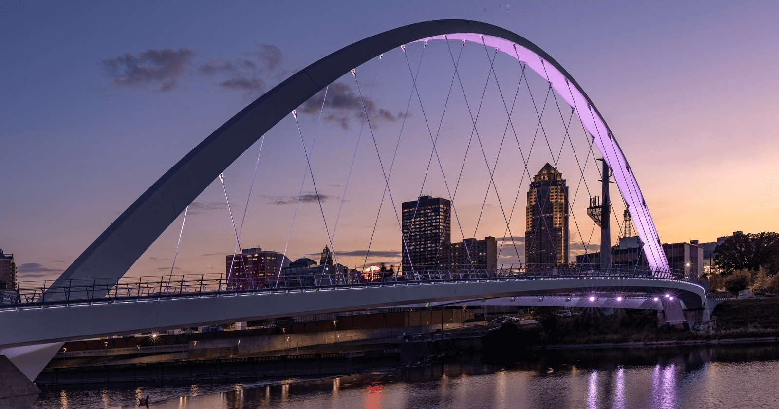 A bridge over a river at dusk with an Iowa skyline in the background.