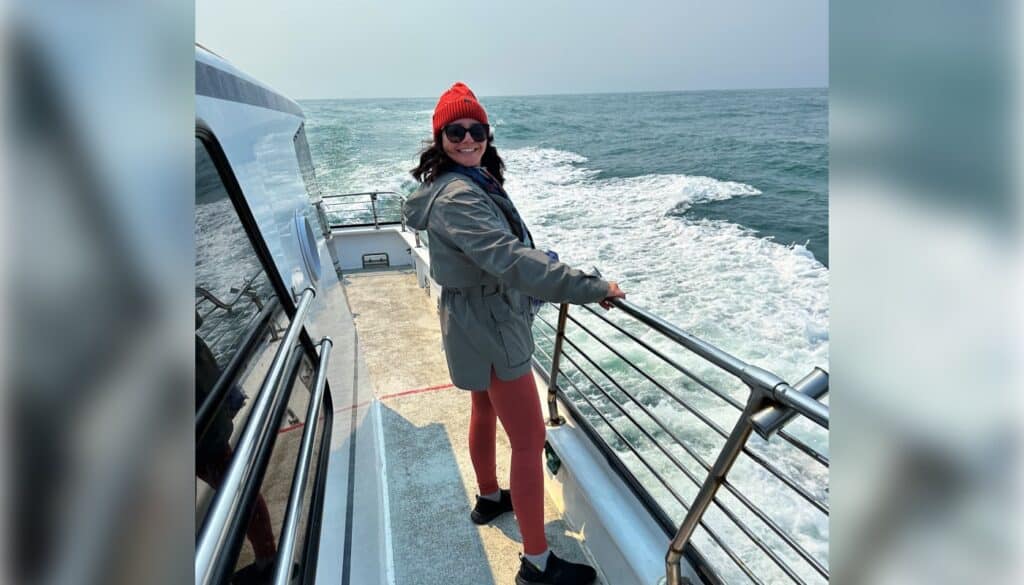 A woman is standing on the railing of a boat.