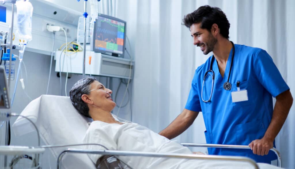 A telemetry nurse on the job adiscussing with a patient in a hospital bed.