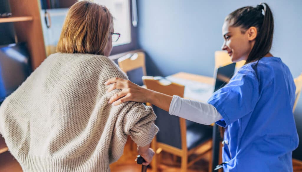 A nurse is helping a woman with a cane.