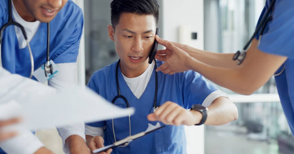 Three medical professionals discussing patient information, with one holding a clipboard.