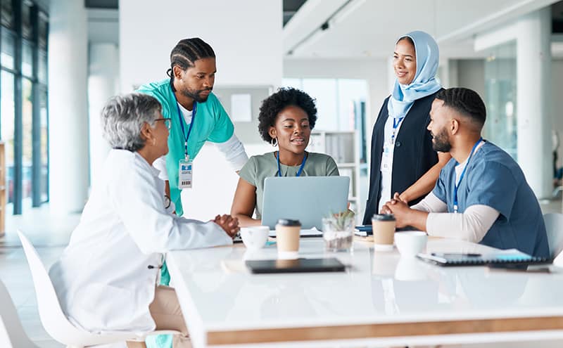 Diverse group of healthcare professionals discussing around a laptop in a modern hospital meeting area.