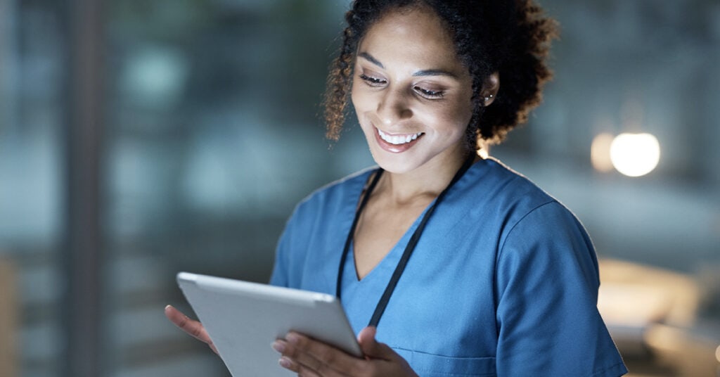 Healthcare professional smiling while looking at a digital tablet.