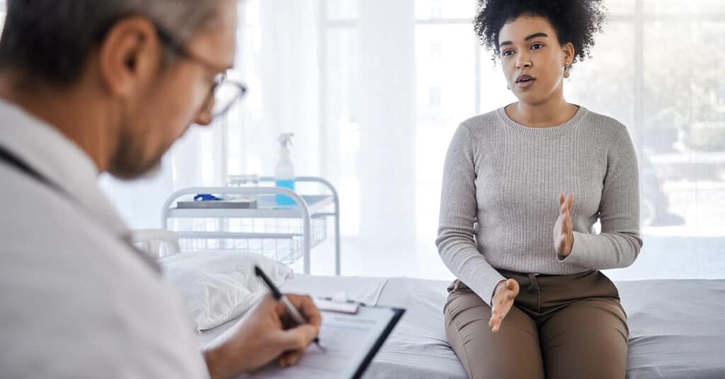 Woman discussing her symptoms with a doctor who is taking notes.